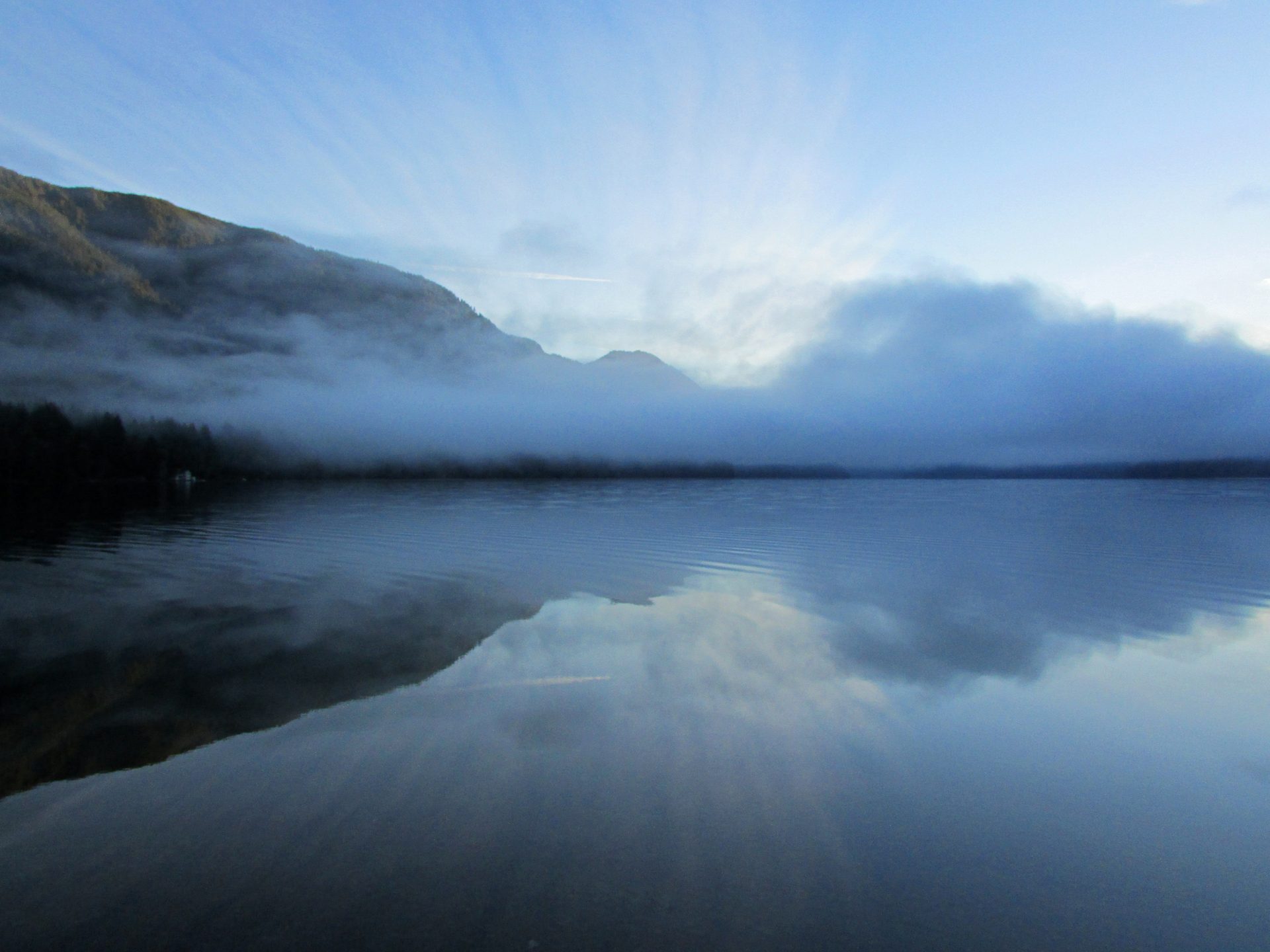 Morning fog drifting over the still, glassy surface of Lake Crescent in Olympic National Park, Washington, with forested ridges reflected in the water