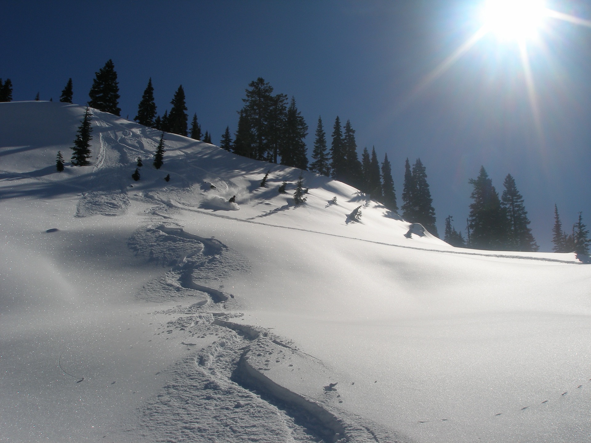 A skier heads downhill on a steep snow-covered slope.