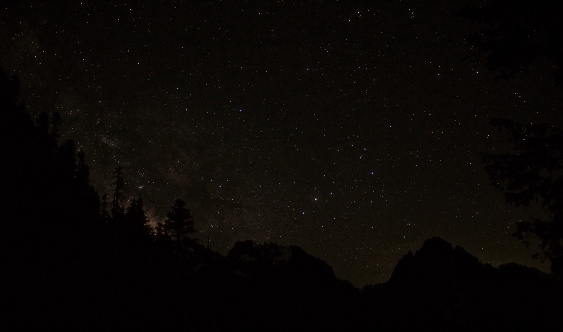 A starry night sky above a ridge of rocky mountain peaks.