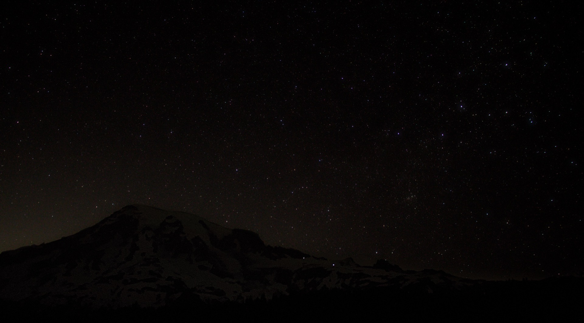 A starry sky stretches above a large volcanic peak.