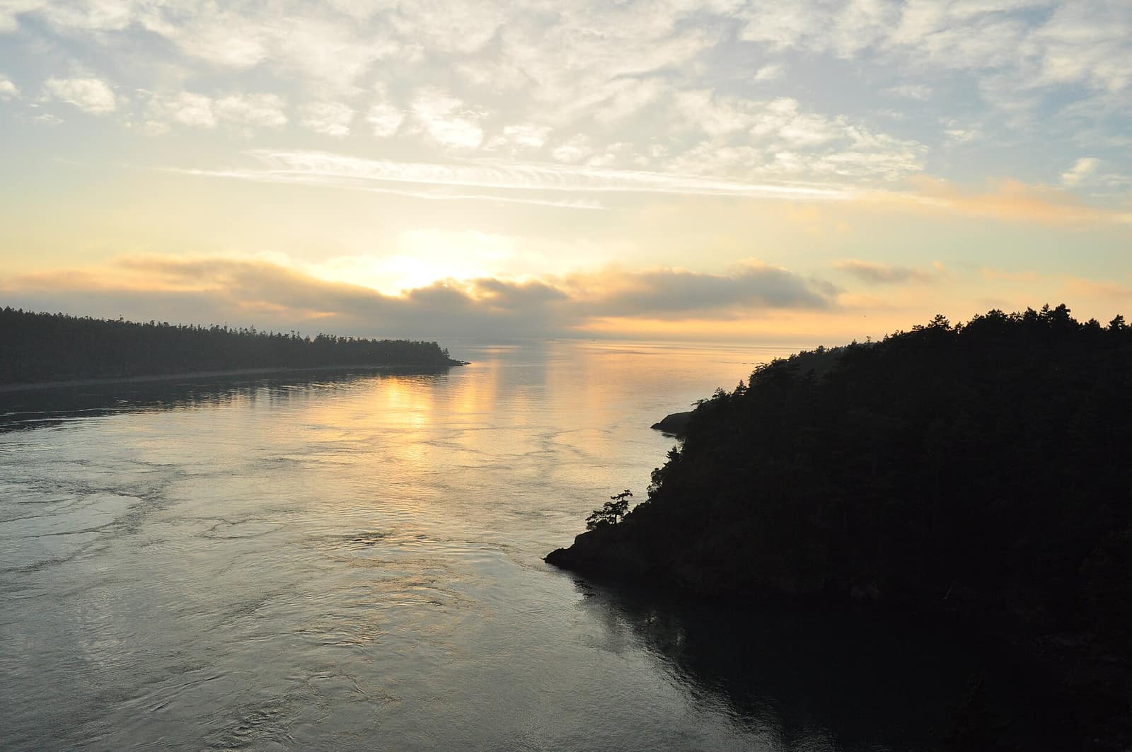 Sunset over the Deception Pass channel seen from the bridge, with forested Whidbey Island shoreline